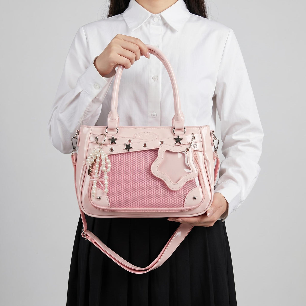 Yume Dual Window Shoulder Ita Bag held by top handles, showing rectangular mesh display window, star-shaped side window, and adjustable shoulder strap